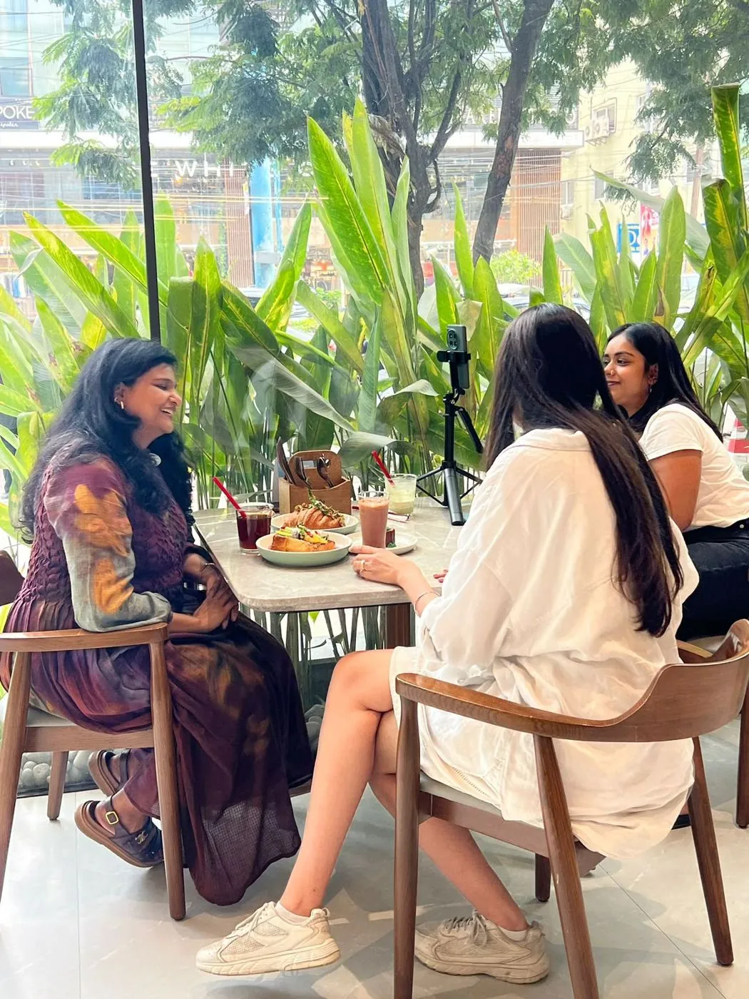 Ayushi in conversation with clients over coffee at a plant-filled cafe